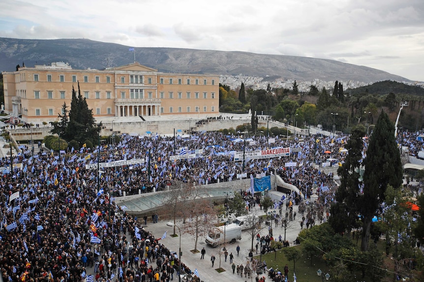 An aerial photo looks out at a u-shaped throng of protesters in front of a sandstone Greek parliament in Athens in the thousands