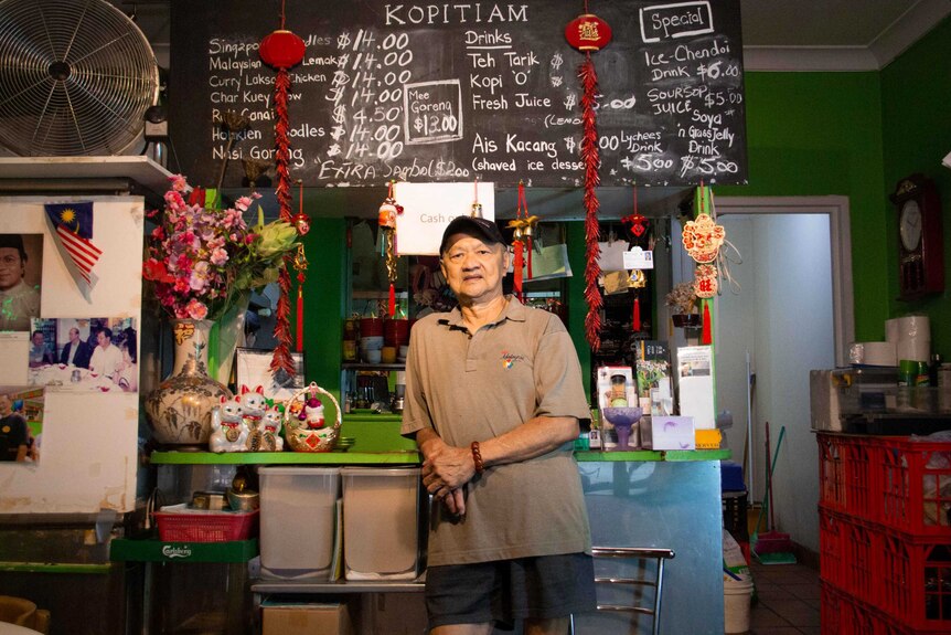 Peter Chan stands inside his  Malaysian restaurant Kopitam Cafe in Sydney with the menu behind him.