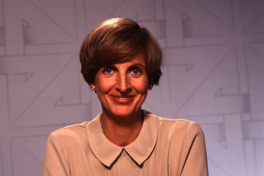 Caroline Jones with a short bob hairstyle sits in front of the Four Corners program backdrop