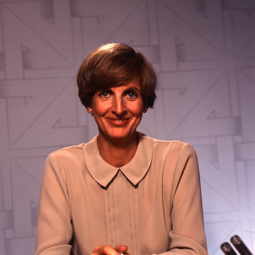 Caroline Jones smiles, behind her is a backdrop for the set of Four Corners.