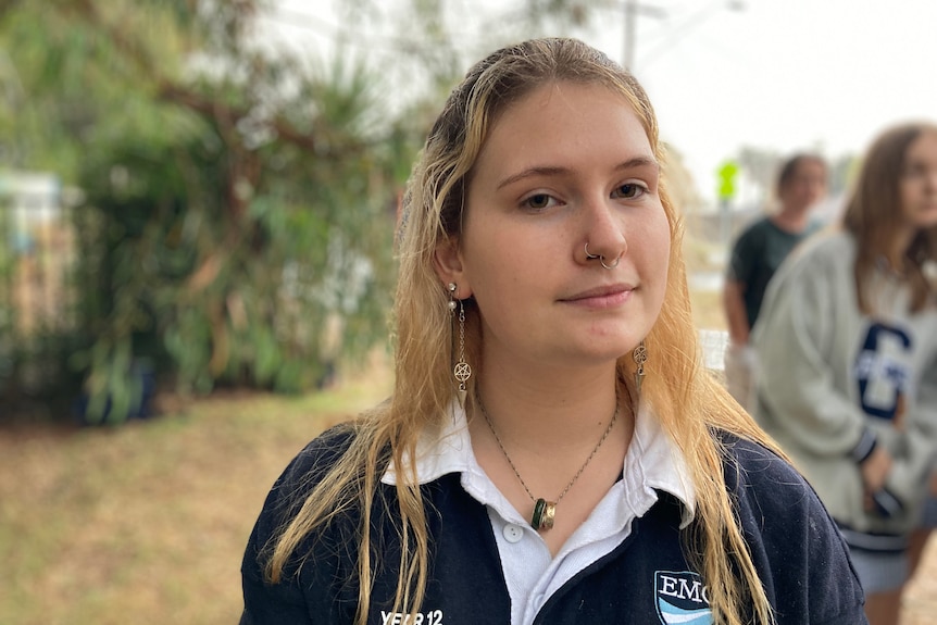 A young woman in school uniform wearing a nose piercing, long earrings and a necklace. 