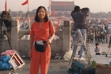 A woman wearing in red standing in the front of tens of thousands of people at Tiananmen Square in Beijing.