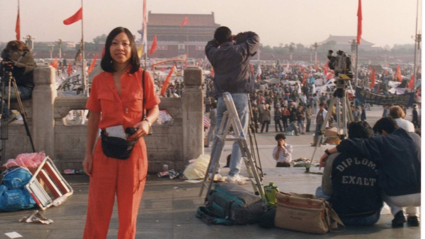 A woman wearing in red standing in the front of tens of thousands of people at Tiananmen Square in Beijing.