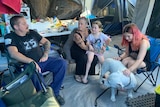 A family - mum, dad, two daughters and a friendly dog sitting in their tent. 