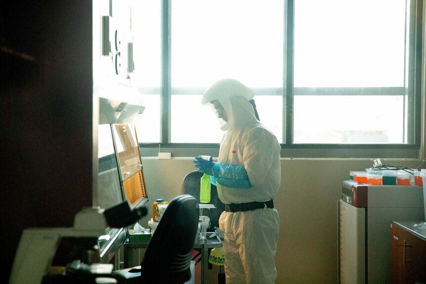 A man in a white hazmat suit looks at a computer in a laboratory 