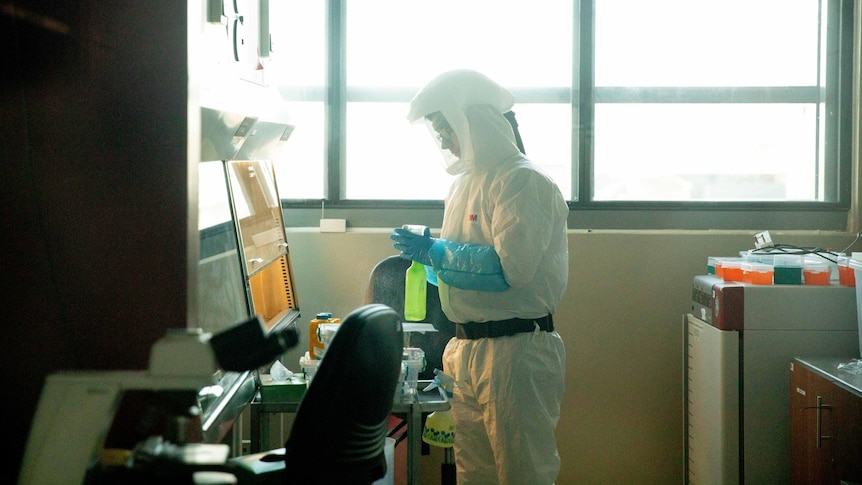 A man in a white hazmat suit looks at a computer in a laboratory 