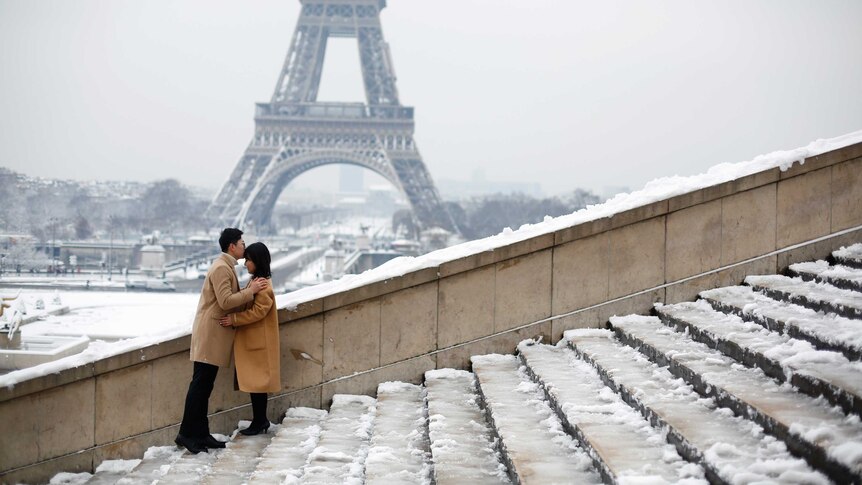 A couple kiss in front of the Eiffel Tower in Paris.