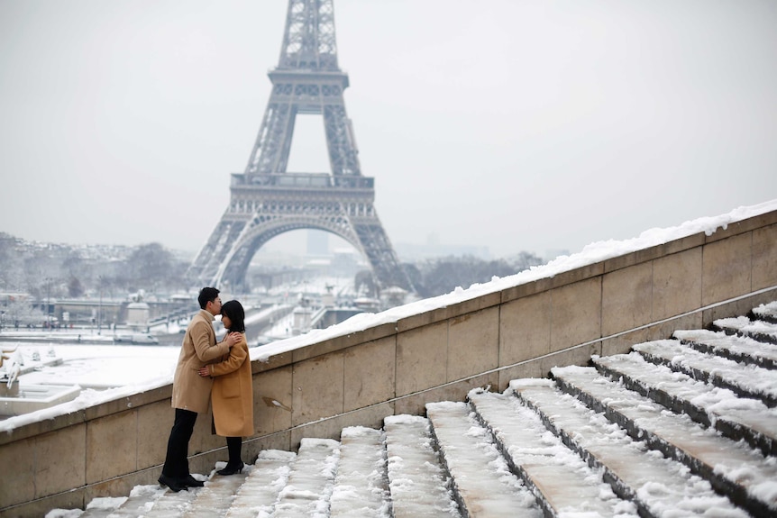A couple kiss in front of the Eiffel Tower in Paris.