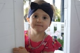 A little girl with a blue headband stands in a doorway.