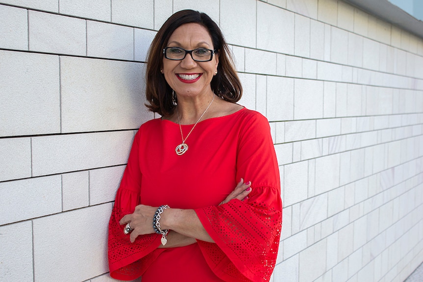 Author Anita Heiss standing with arms crossed in front of a white wall.