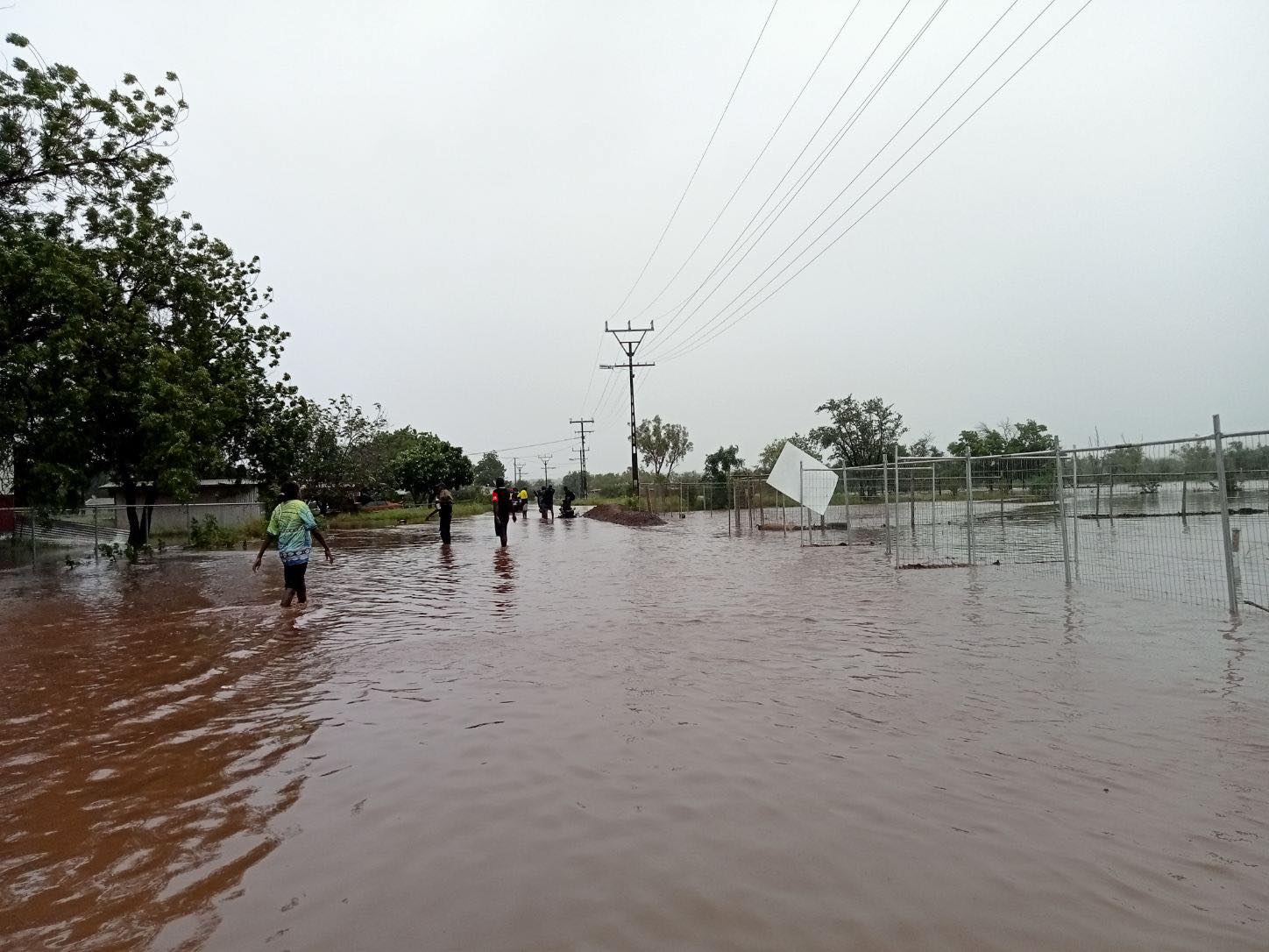 Several people walking through a heavily flooded roadway in a remote community.