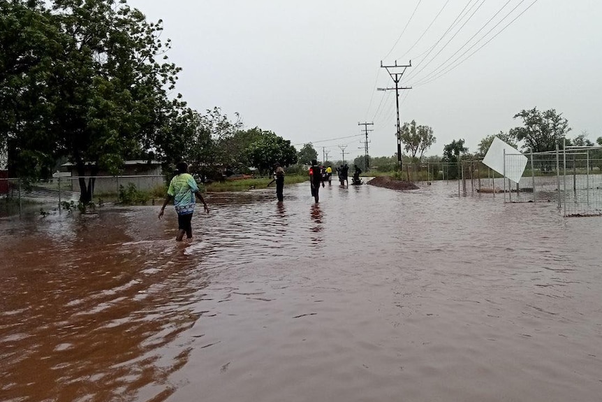 Several people walking through a heavily flooded roadway in a remote community.