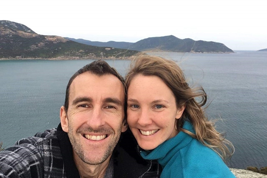 A man and a woman smiling at the camera with the sea in the background.