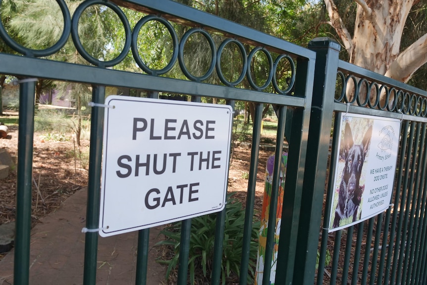 A school fence affixed with a sign that reads "shut the gate".
