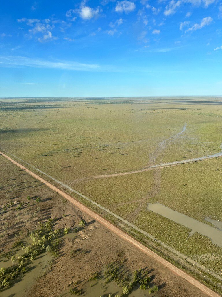 An aerial shot of grassy brown outback and blue sky.