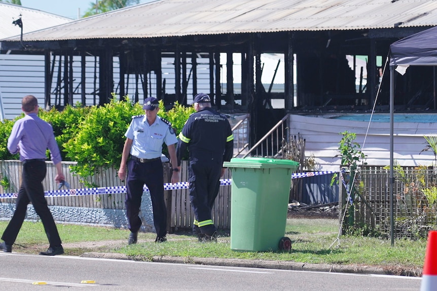 A police officer and fire fighter stand outside a burnt-out home surrounded by police tape