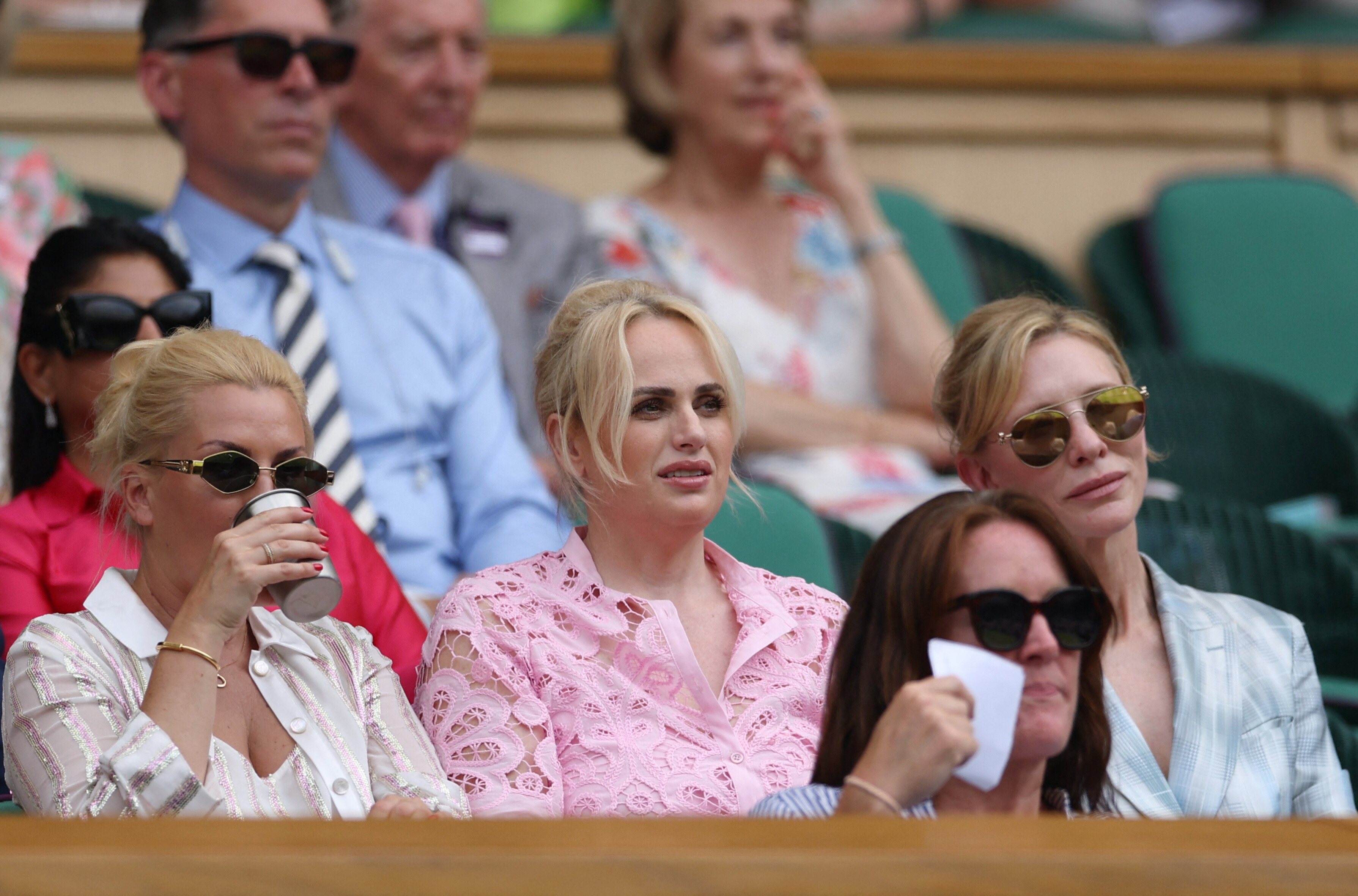 Three blonde women watch the tennis in sunglases and pastel colours