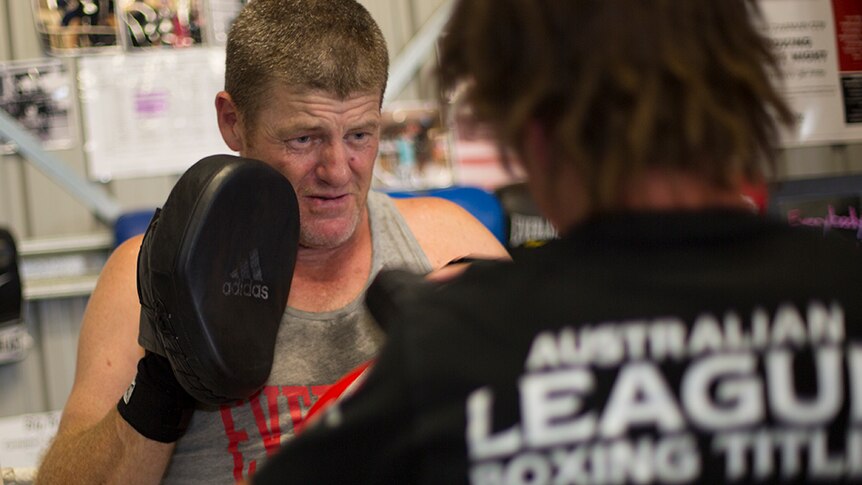 Boxing coach Scott Griffiths wears pads on his hands to take hits from a training partner in the gym.