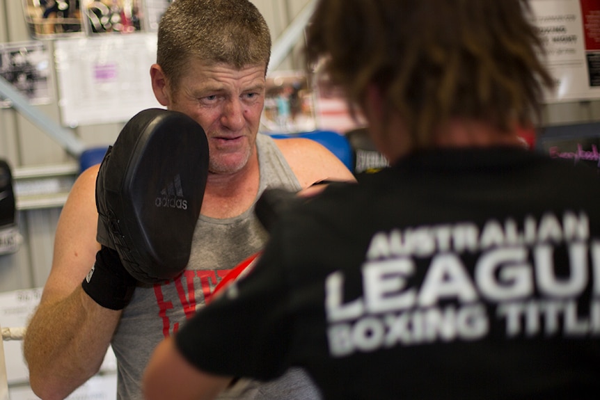 Boxing coach Scott Griffiths wears pads on his hands to take hits from a training partner in the gym.