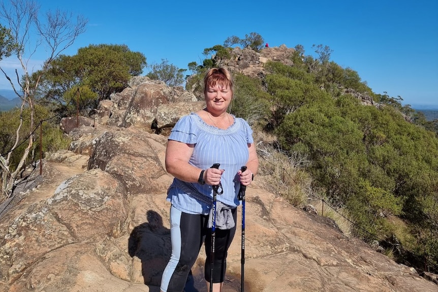 a woman smiles at the camera on a rocky path holding hiking sticks