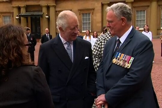 King Charles speaks to a man in a suit decorated with medals