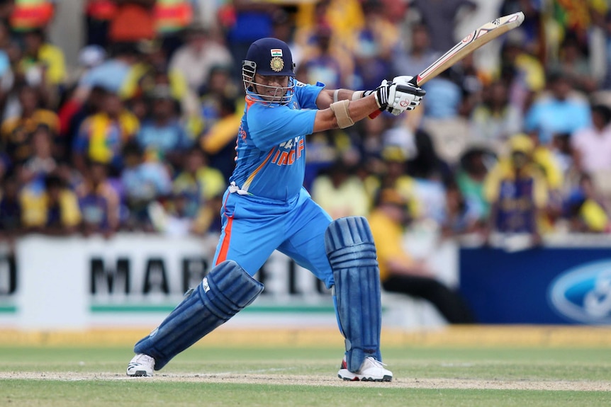 A cricket player completes a shot, with his bat raised at a 30 degree angle out in front of him, arms straight.