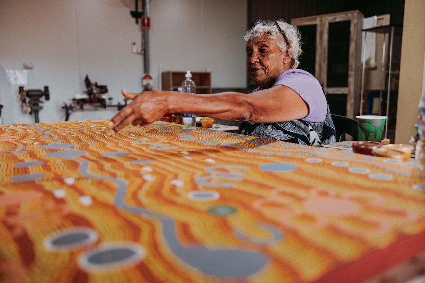 An Indigenous elder works on a large traditional painting.