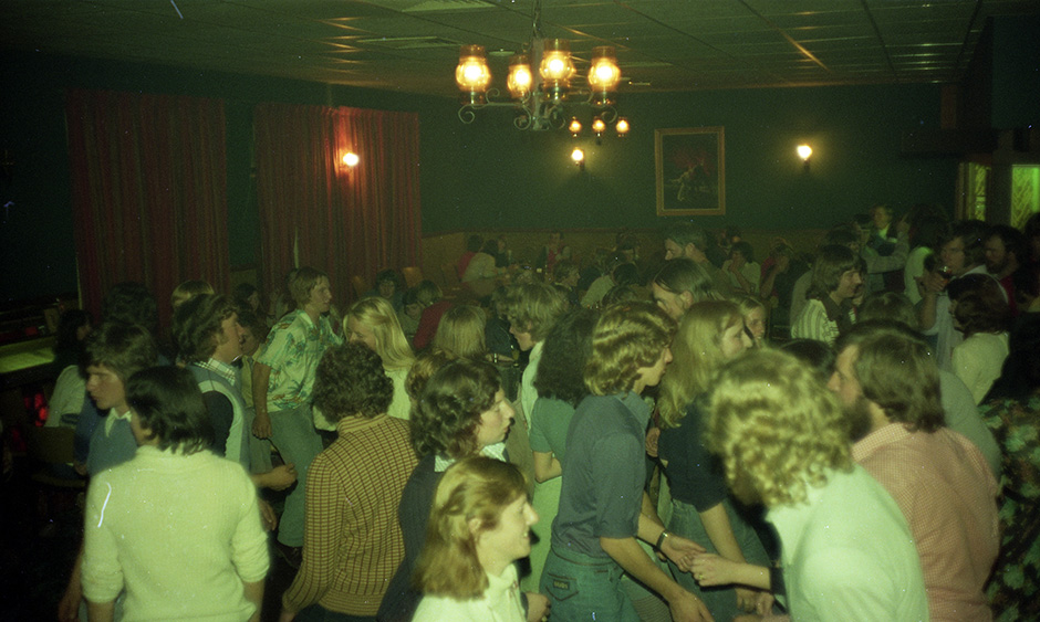 Old photo of a crowd of young people dancing in a smoky pub room.