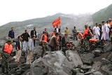 Emergency workers in high-visibility jackets and army fatigues stand on boulders unleashed by the landslide.