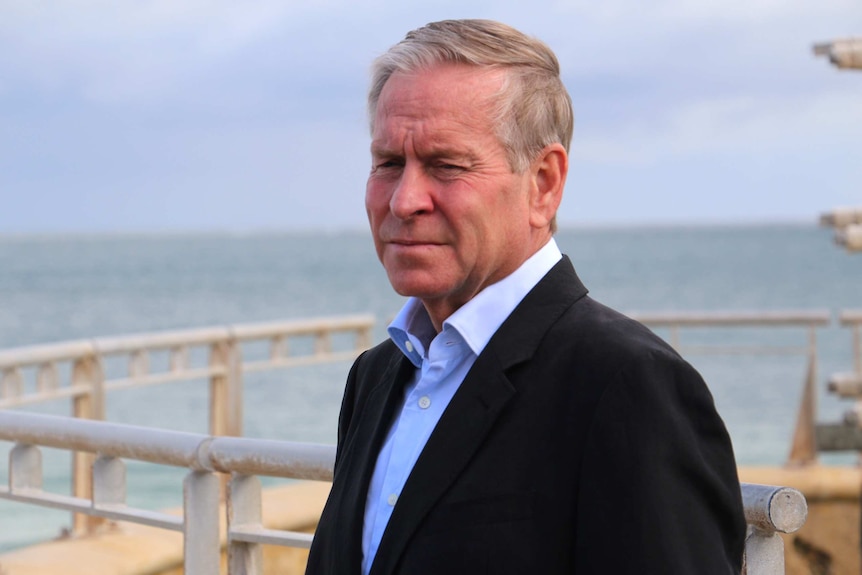 A midway shot of Colin Barnett gazing into space standing in front of Sorrento Beach.