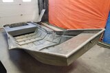 An aluminium boat, bent upwards in the middle, sitting on a concrete floor.
