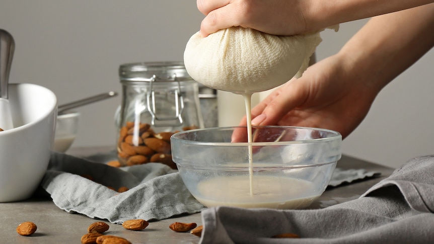 A close-up of someone making almond milk by straining soaked nut pulp through a cloth into a small bowl.