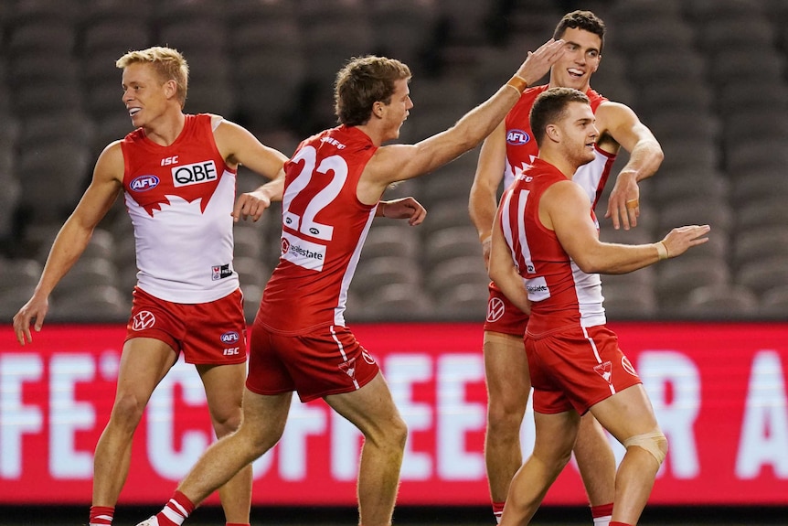 An AFL player celebrates his goal as a group of his teammates smile and congratulate him.