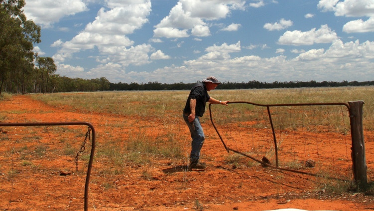 A man closes a gate in a paddock with red dirt.