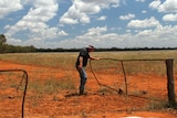 A man closes a gate in a paddock with red dirt.