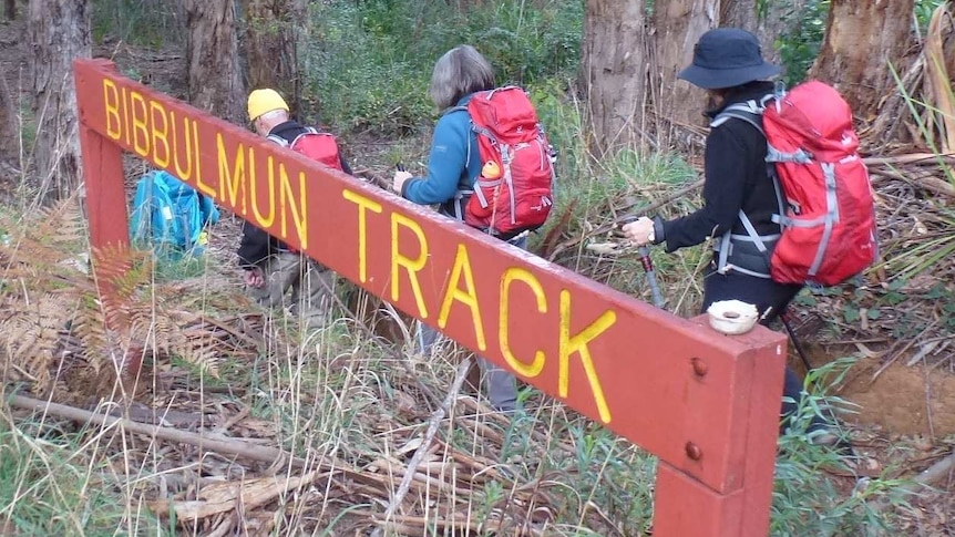 Hikers walk through bushland with a sign for the Bibbulmun Track in the foreground