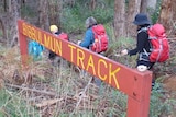 Hikers walk through bushland with a sign for the Bibbulmun Track in the foreground