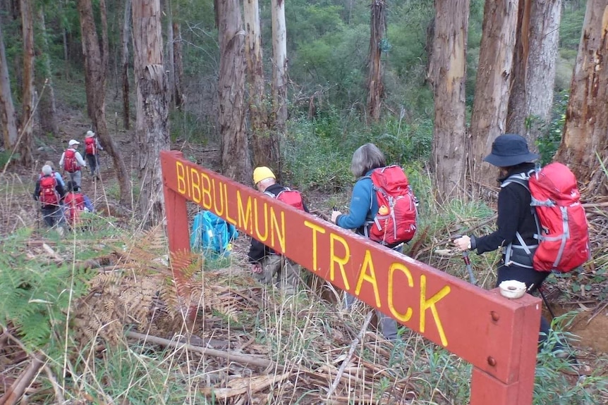 Hikers walk through bushland with a sign for the Bibbulmun Track in the foreground