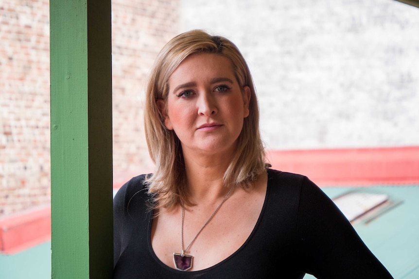 Grace Rullis standing on a balcony, she is wearing a black top and has blonde hair.