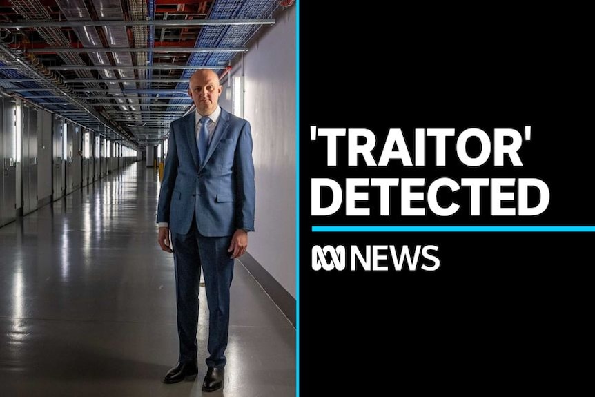 'Traitor' Detected: Man in blue stands in a stark corridor with exposed wiring overhead