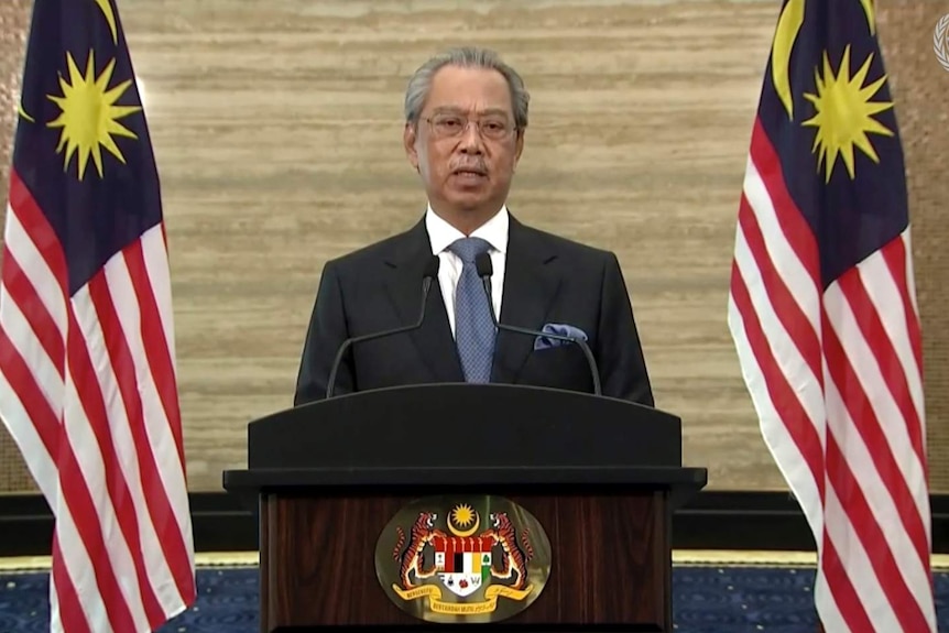 Malaysian Prime Minister Muhyiddin Yassin makes a speech alongside two Malaysian flags.