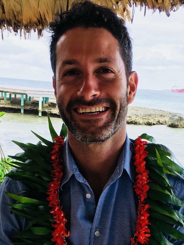 Man smiles at camera while wearing lei.