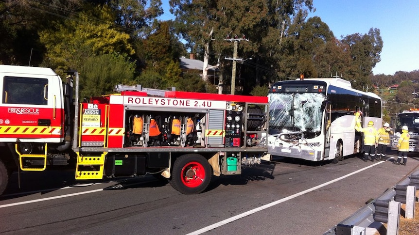 The front windscreen of a white school bus is completely smashed after hitting the back of a firetruck.