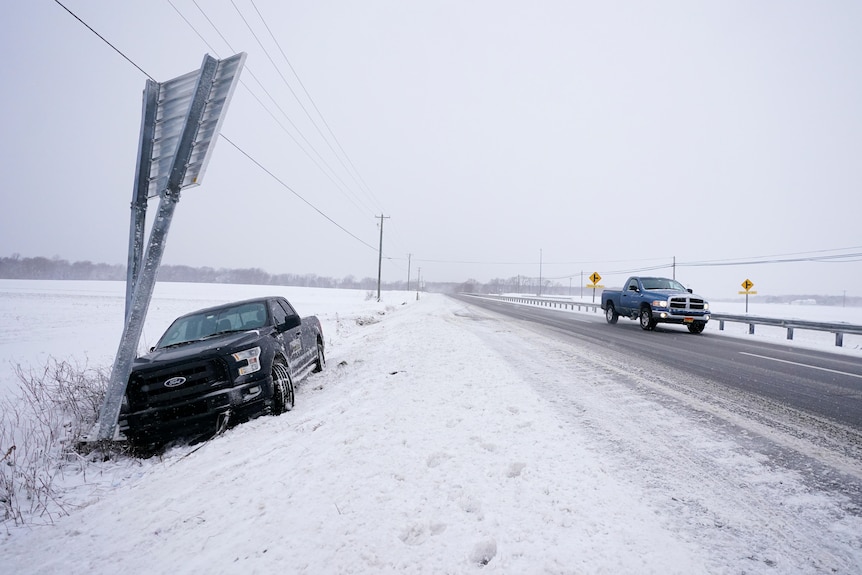 An abandoned vehicle is seen at the spot where it crashed onto a sign by the side of a snow covered highway.
