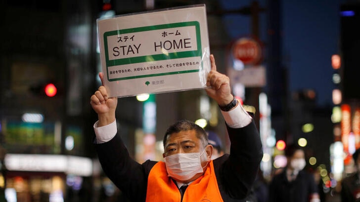 A Japanese man holding up a sign which says "Stay Home"