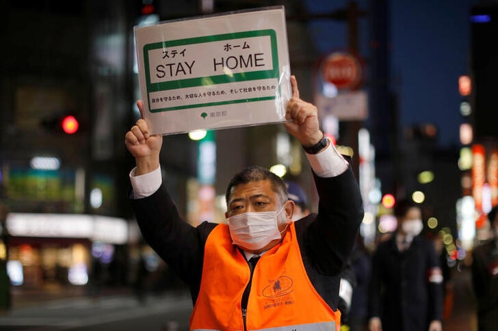 A Japanese man holding up a sign which says "Stay Home"