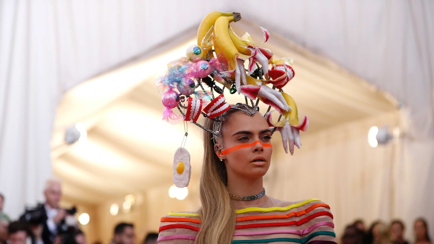 Cara Delevingne at the MET Gala wearing a hat featuring bananas, plastic teeth and fake fried eggs.