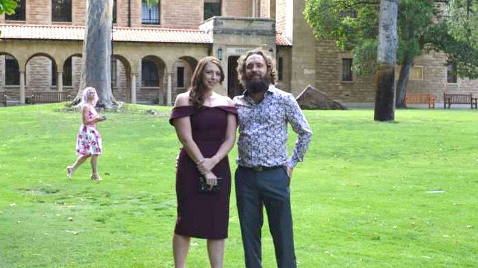 Perth man Michael Kearns, 33, and his British partner Louise Benson stand in a park posing for a photo and smiling.