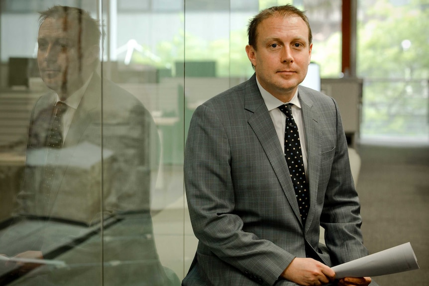 Charles Bannister sits near a glass wall which reflect his image.