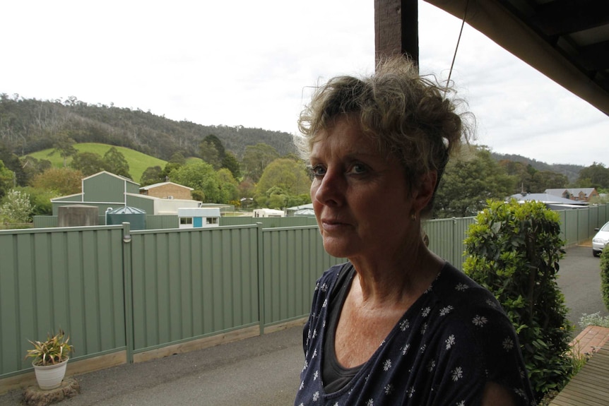 A woman stands in her backyard, with lush hills and bushland visible over her back fence.
